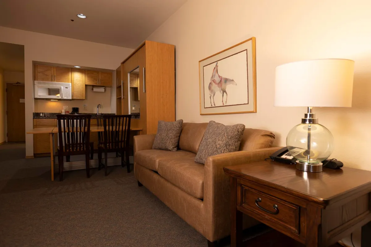 An open interior view of a living and dining area featuring a plush sofa, a stylish dining table, and framed artwork. Soft, natural light streams in through windows, enhancing the comforting, relaxed ambiance ideal for unwinding or socializing.