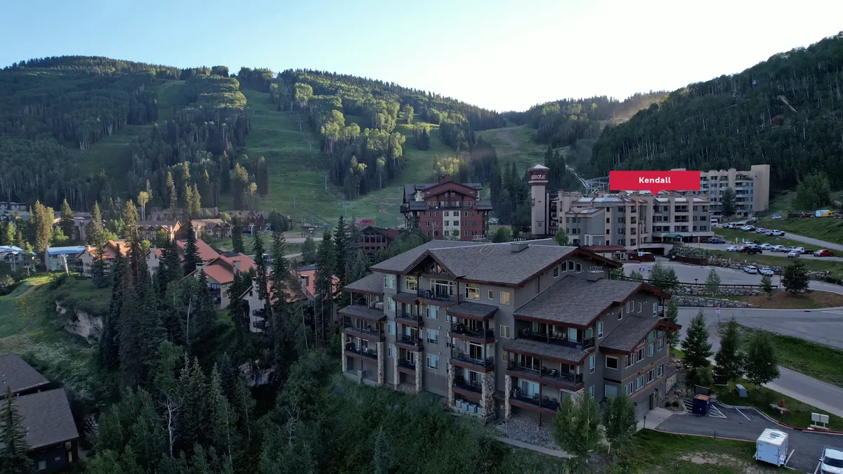 This exterior shot presents the resort buildings set against a stunning mountain backdrop, with pine trees dotting the landscape. The tranquil setting visually communicates the sense of retreat and seclusion promised by the suite's private sanctuary theme.
