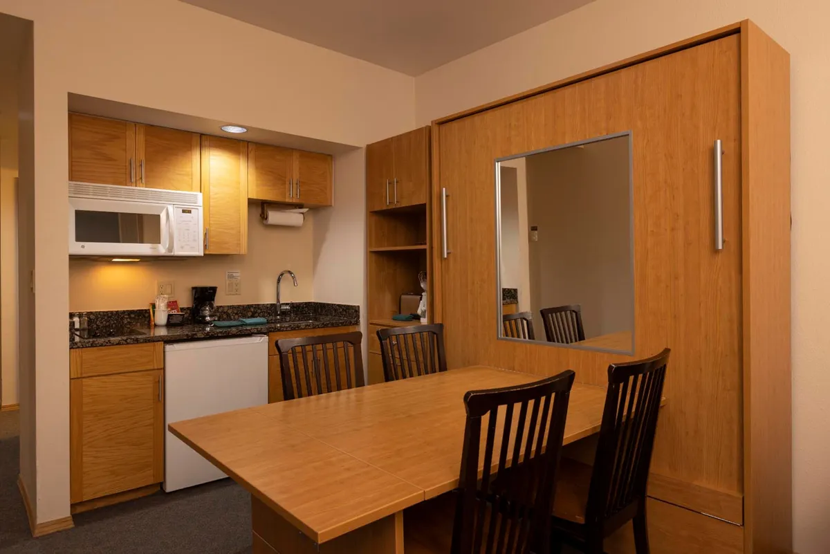 This image showcases the heart of the home: a cozy kitchen with modern wooden cabinetry, an inviting dining table, and a seamless open layout ideal for both meal preparation and socializing. The kitchen area is visually connected to the dining space, highlighting how the area supports both cooking and gathering.