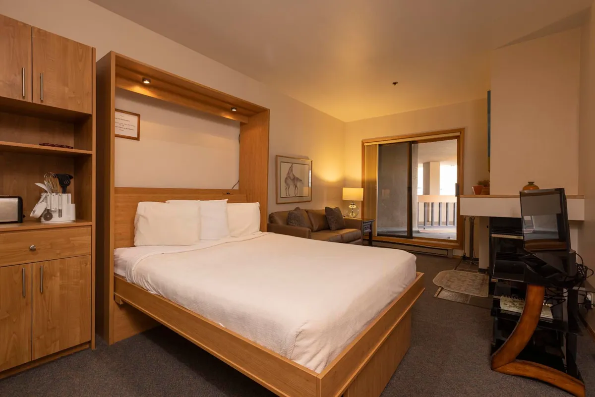 A combined bedroom and lounge area with a seating nook and direct access to an outdoor patio via sliding doors. The space is filled with soft textures and warm lighting, creating a peaceful retreat perfect for unwinding after a day of adventure.