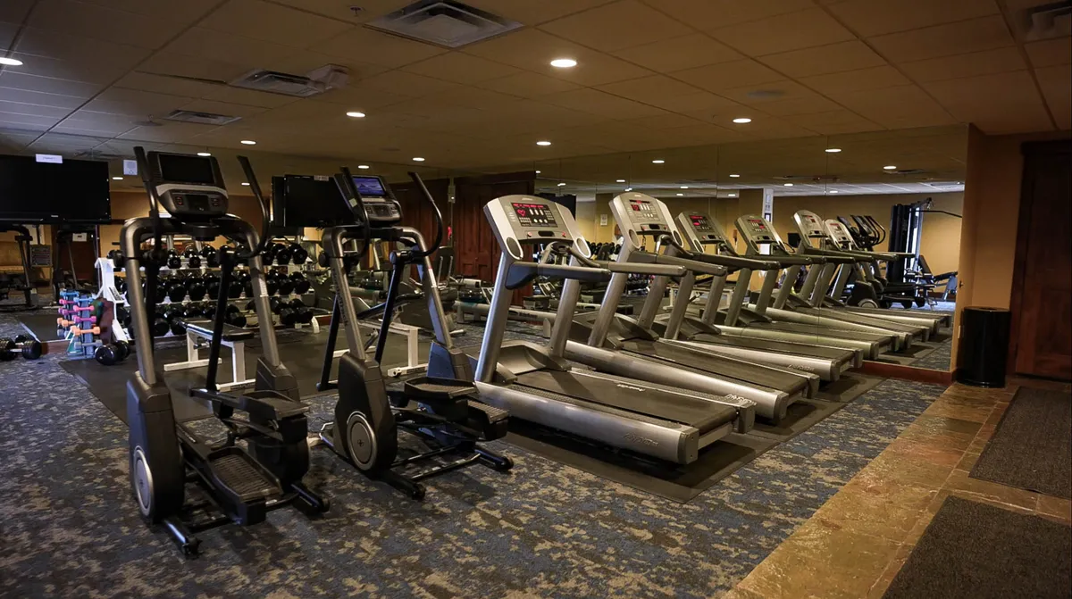 A modern, well-equipped fitness center featuring treadmills, elliptical machines, dumbbells, and a mirrored wall. The room is bright and organized, inviting guests to keep up with their fitness routines.